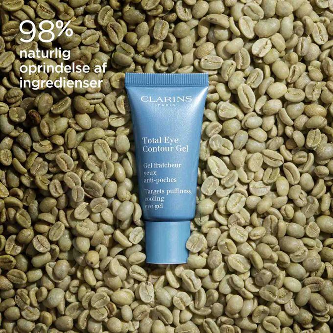 Tube of Clarins Total Eye Contour Gel among coffee seeds to illustrate the natural origin of the product's ingredients.