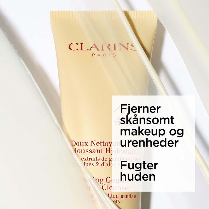 Packshot af den gule tube med fugtgivende mild skummende rens placeret ved siden af gul ensian og aloe vera p&aring; en lysegul baggrund.
