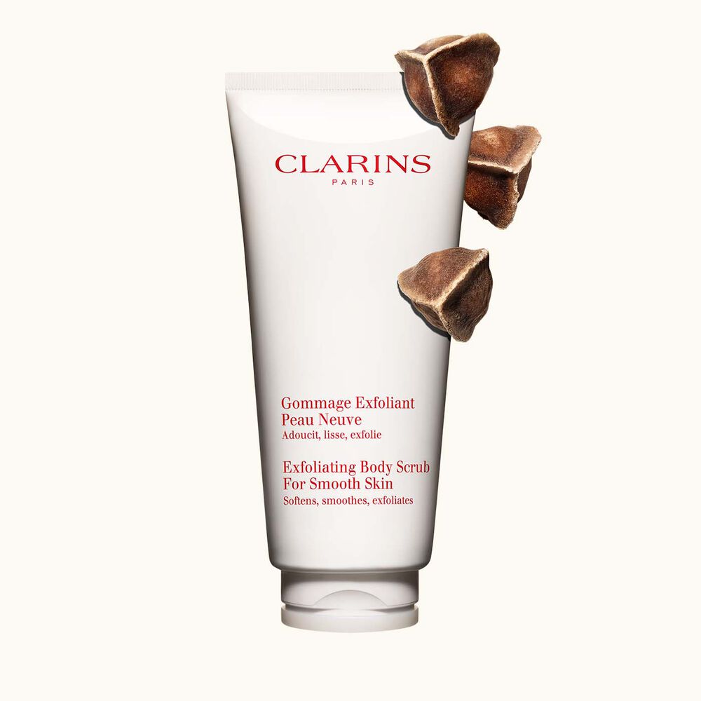 Packshot of Clarins Exfoliating Body Scrub for Smooth Skin placed next to moringa nuts on a light beige background