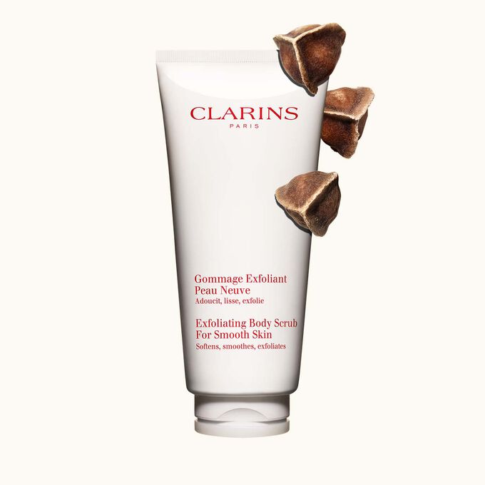 Packshot of Clarins Exfoliating Body Scrub for Smooth Skin placed next to moringa nuts on a light beige background