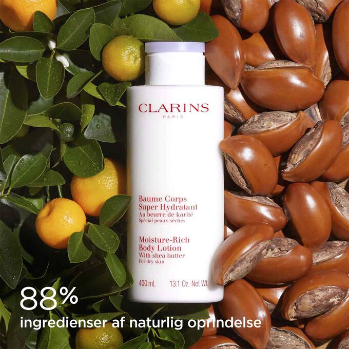 Bottle of Clarins Moisture-Rich Body Lotion surrounded by shea nuts and oranges, to illustrate its natural ingredients.