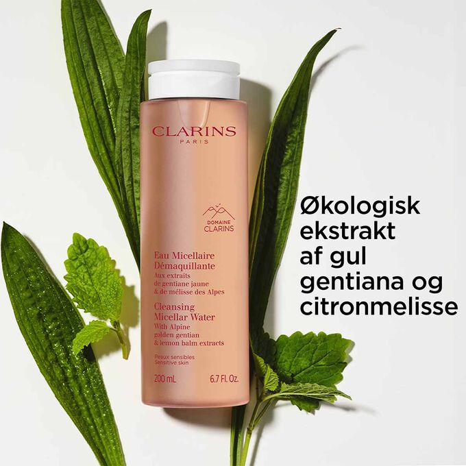 Packshot af flasken med rensende micellarvand foran citronmelisse og gul gentiana for at fremh&aelig;ve dens hovedingrediens.