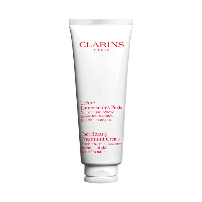Packshot of a bottle of Clarins Foot Beauty Treatment Cream close to some shea nuts on a white background.