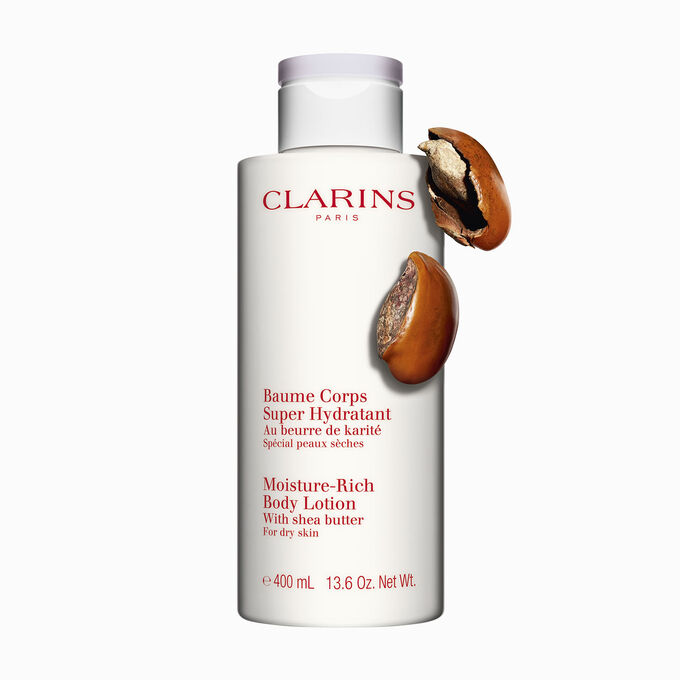 Packshot of a bottle of Clarins Moisture-Rich Body Lotion close to some shea nuts on a white background.