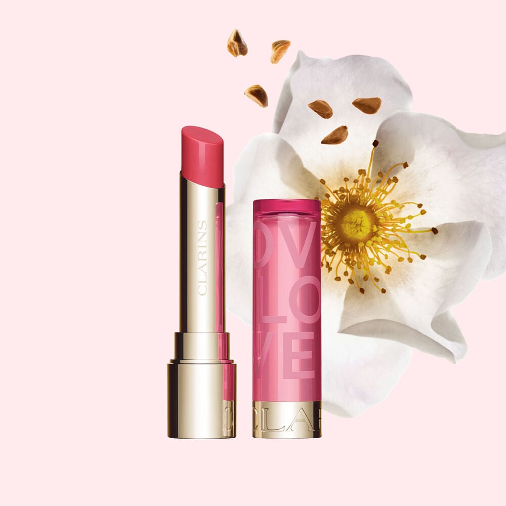Packshot af Lip Balm Limited Edition Love Collection foran en rose p&aring; en lyser&oslash;d baggrund, der fremh&aelig;ver dens livlige farve.