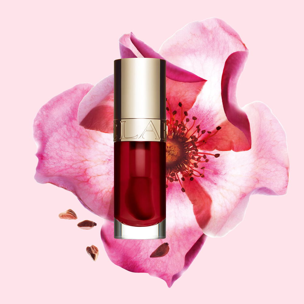 Packshot af Clarins Lip Comfort Oil i Cherry, placeret ved siden af en nyponrose p&aring; en lys rosa baggrund.