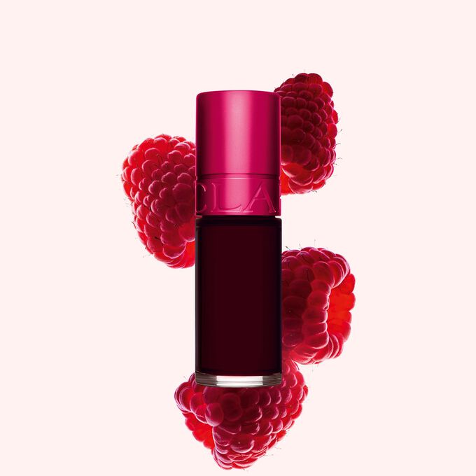 Packshot af Clarins Pink Water Lip Stain i nuance 04, placeret ved siden af hindbær på en lyserød baggrund.