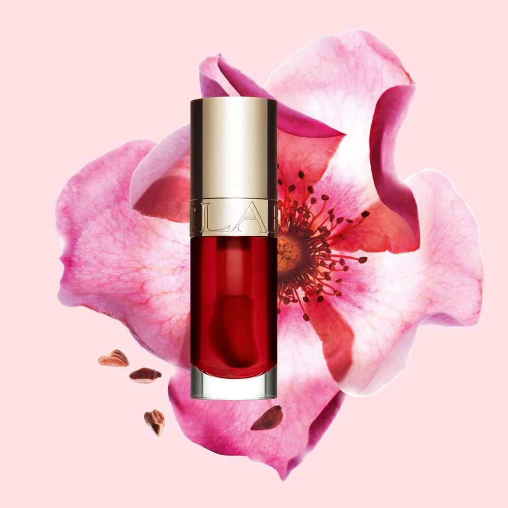 Packshot af Clarins Lip Comfort Oil Strawberry, placeret ved siden af en nyperose p&aring; en lyser&oslash;d baggrund.
