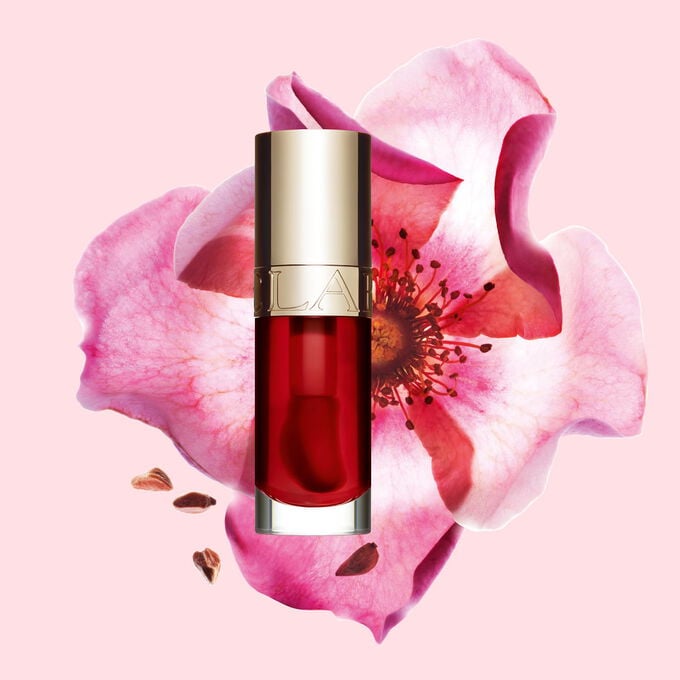 Packshot af Clarins Lip Comfort Oil Strawberry, placeret ved siden af en nyperose p&aring; en lyser&oslash;d baggrund.