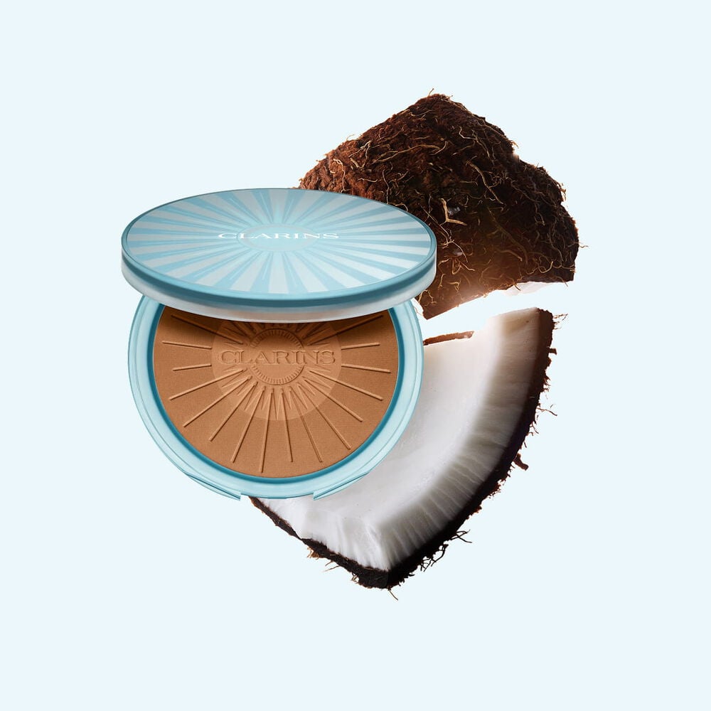 Packshot af Summer Bronzing Powder omgivet af kokos, der illustrerer dens n&oslash;gleingrediens for en naturlig, solkysset gl&oslash;d