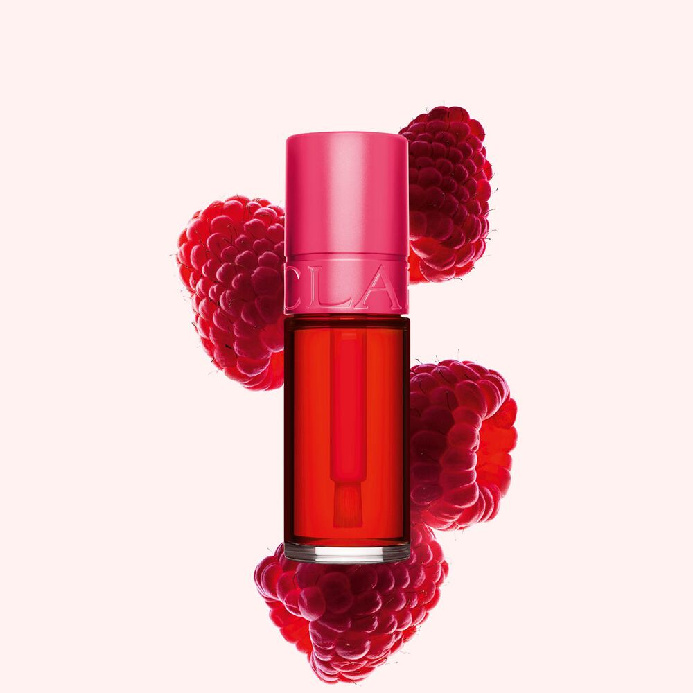 Packshot af Clarins Fushia Water Lip Stain i nuance 01, placeret ved siden af hindbær på en lyserød baggrund.