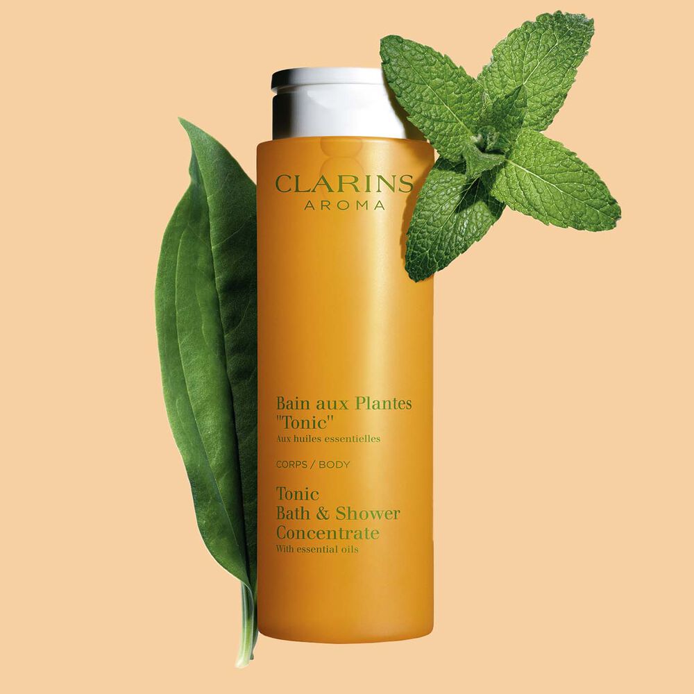 Packshot of Clarins Tonic Bath and Shower Concentrate gel, close to some mint and rosemary leaves on a orange background.