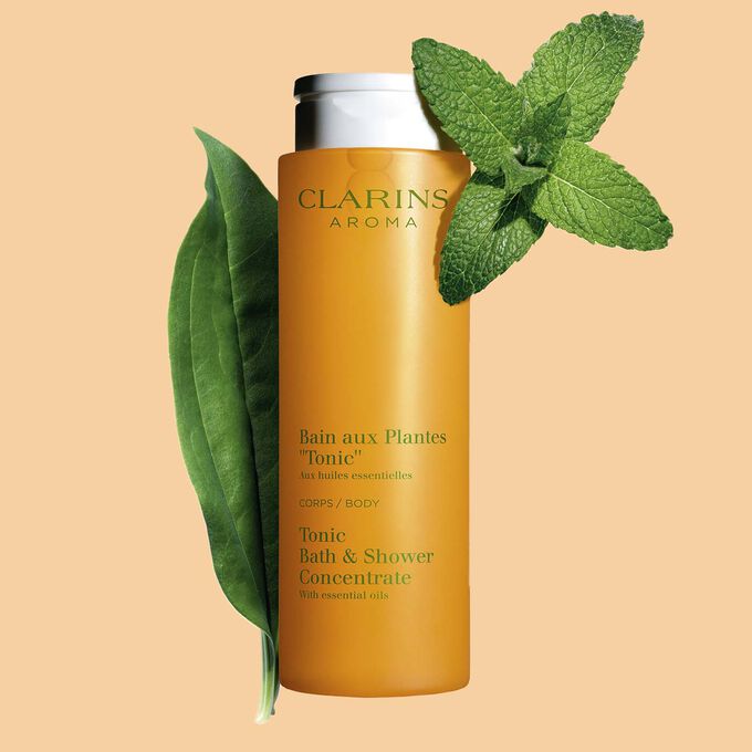 Packshot of Clarins Tonic Bath and Shower Concentrate gel, close to some mint and rosemary leaves on a orange background.