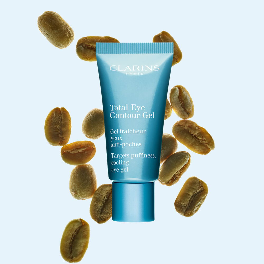 Packshot of a tube of the Total Eye Contour Gel by Clarins close to coffee seeds on a blue background.