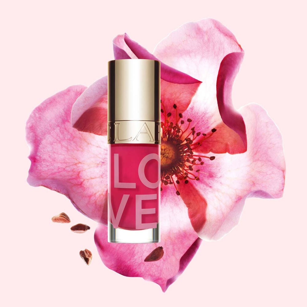 Packshot af Lip Oil Limited Edition Love Collection foran en rose p&aring; en lyser&oslash;d baggrund, der fremh&aelig;ver dens livlige farve.