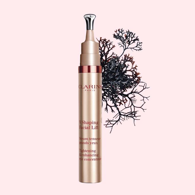 Packshot of a tube of the V Shaping Facial Lift Eye by Clarins close to irish moss on a light pink background.