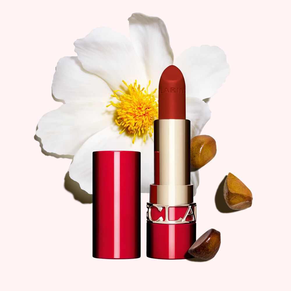 Packshot af Clarins mat læbestift Joli Rouge 782 V, ved siden af kamelia-blomst og sheafrø på lyserød baggrund.