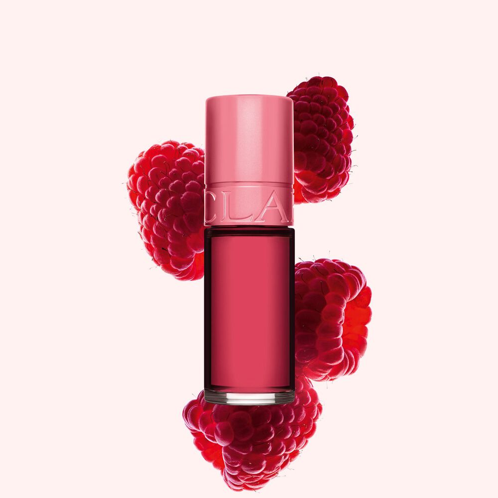 Packshot af Clarins Pink Water Lip Stain i nuance 11, placeret ved siden af hindbær på en lyserød baggrund.