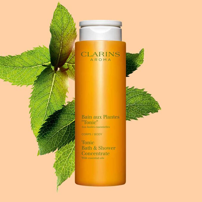Packshot of Clarins Tonic Bath and Shower Concentrate gel, close to some mint and rosemary leaves on a orange background.