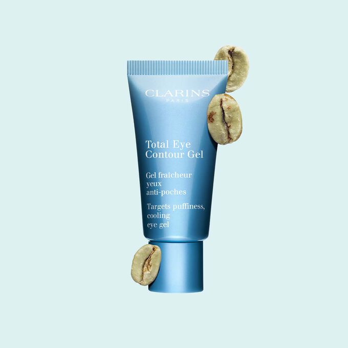 Packshot of a tube of the Total Eye Contour Gel by Clarins close to coffee seeds on a blue background.