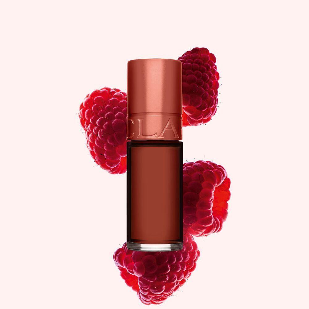 Packshot af Clarins Brown Water Lip Stain i nuance 13, placeret ved siden af hindbær på en lyserød baggrund.