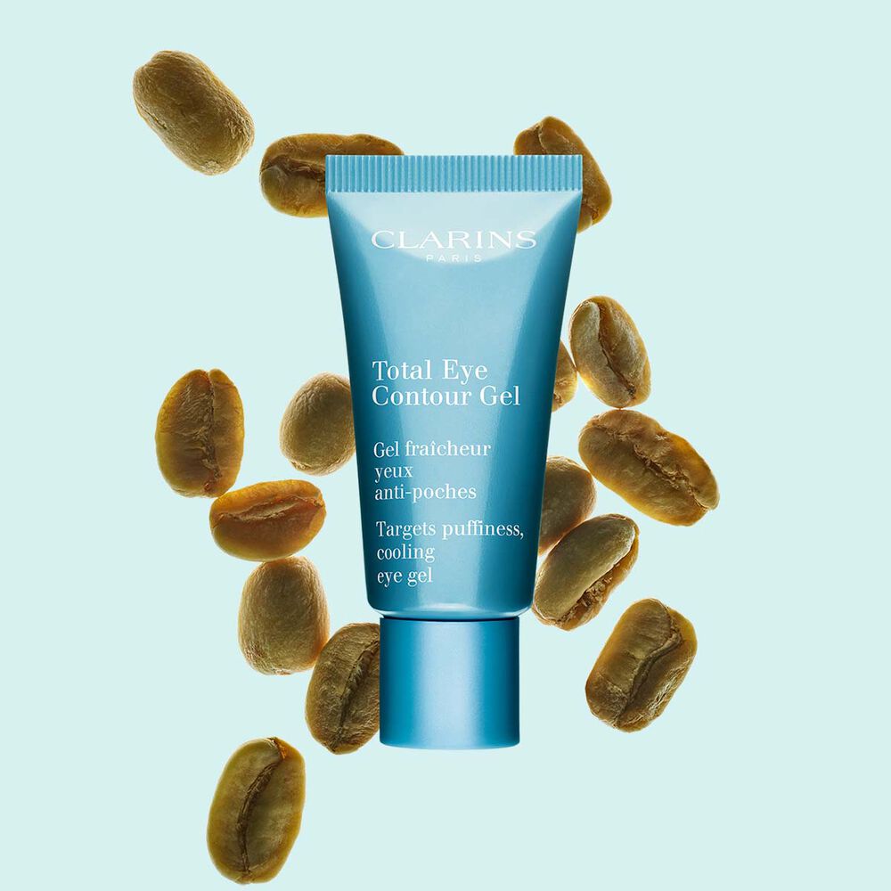 Packshot of a tube of the Total Eye Contour Gel by Clarins close to coffee seeds on a blue background.